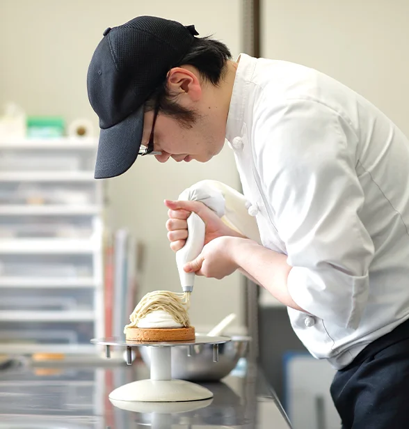 パティシエが白いクリームのケーキに絞り袋で飾りを加えている手元