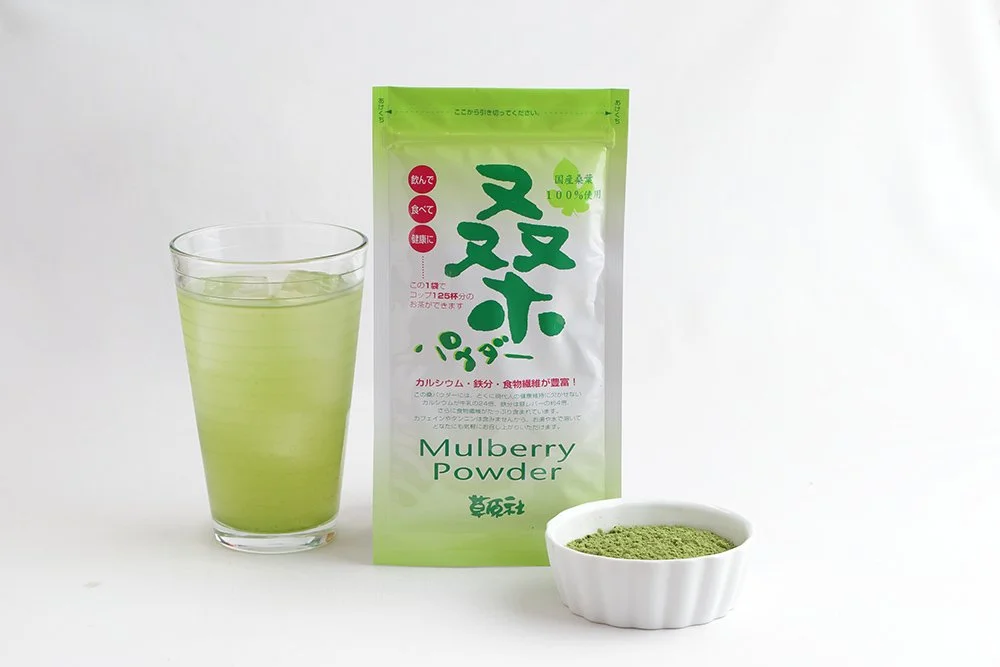 桑パウダーを溶かした緑色の飲み物と桑パウダーのパッケージ、白い器に盛られた粉末